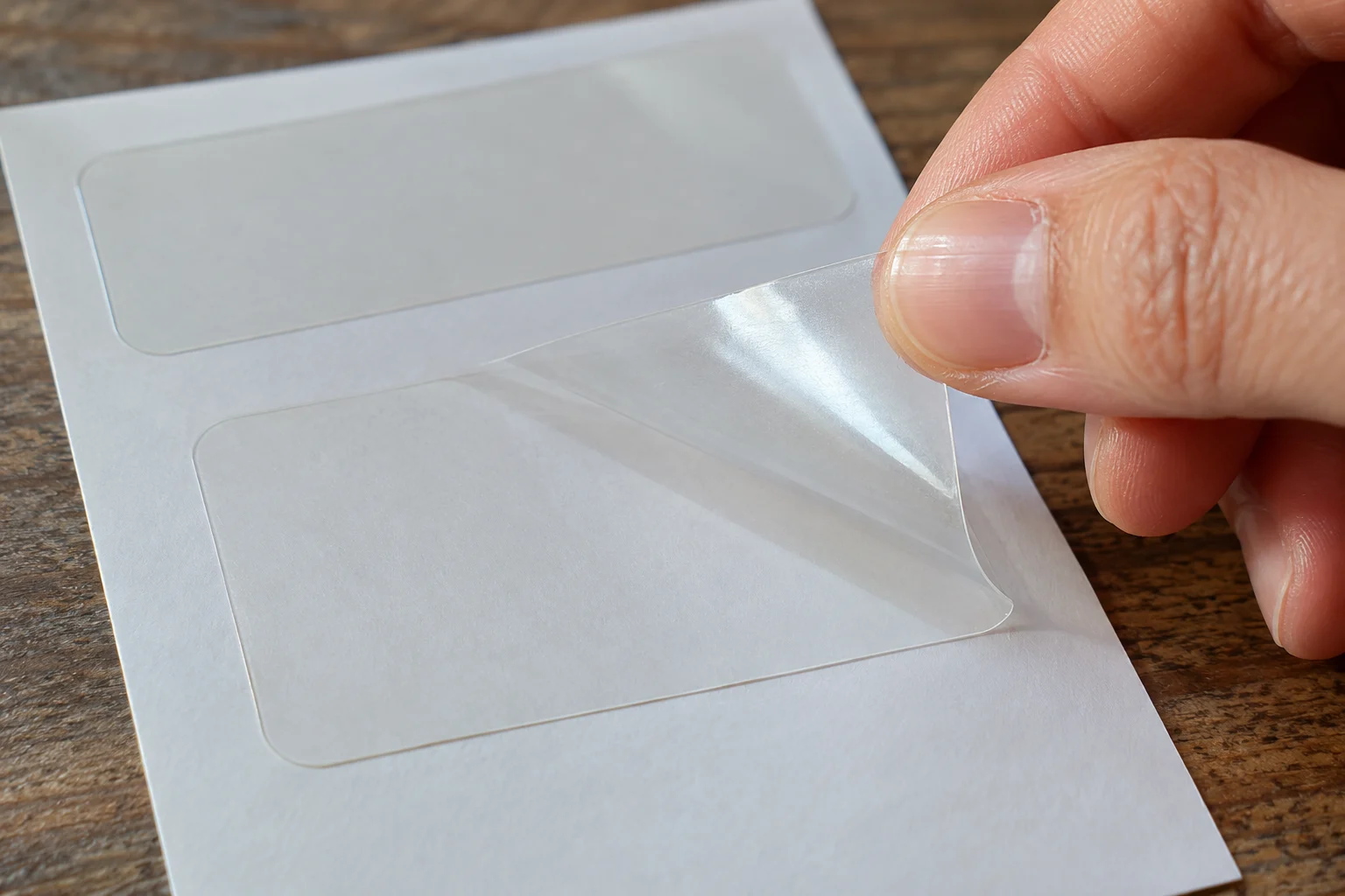Detalhe de uma etiqueta transparente sendo retirada do liner branco